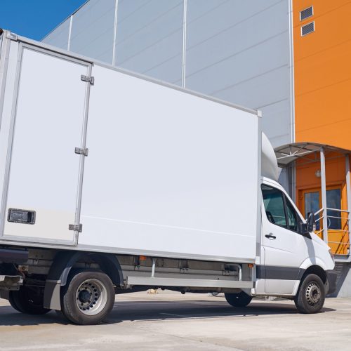Car, warehouse. White cargo covered vehicle standing outdoors in parking lot near warehouse on fine day